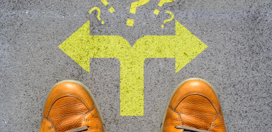 Looking down at a pair of men's feet in shoes and arrows showing a choice to go left or right